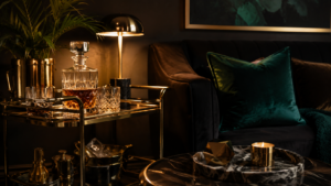 moody editorial flatlay of neo deco home decor — brass bar cart, sunburst mirror, emerald velvet and geometric tray — neo deco home decor 2026